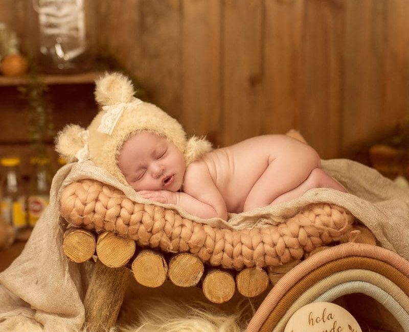 Foto bebé recién nacido con fondo amarillo y madera en un sesión de fotos de Alejandra Mato Fotografía